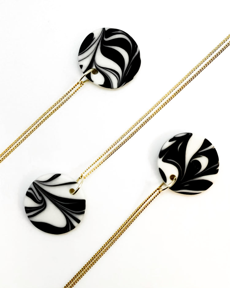 Black and white marbled earrings with gold chains on a white background