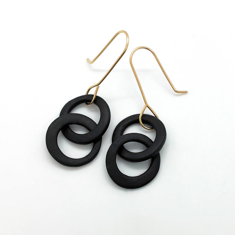 Black circular earrings on gold hooks against a white background