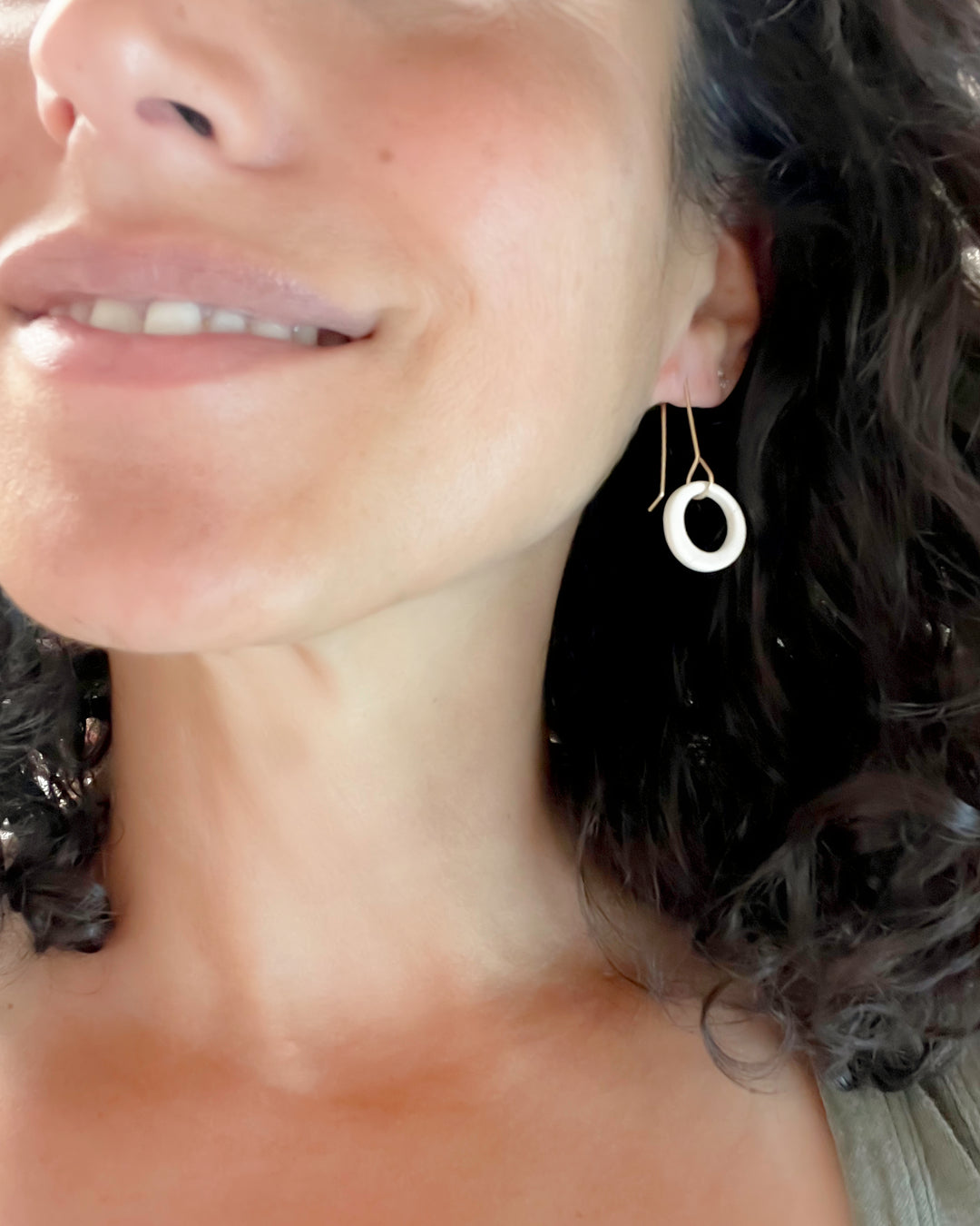 Close-up of a woman wearing a gold and white earring with a circle.
