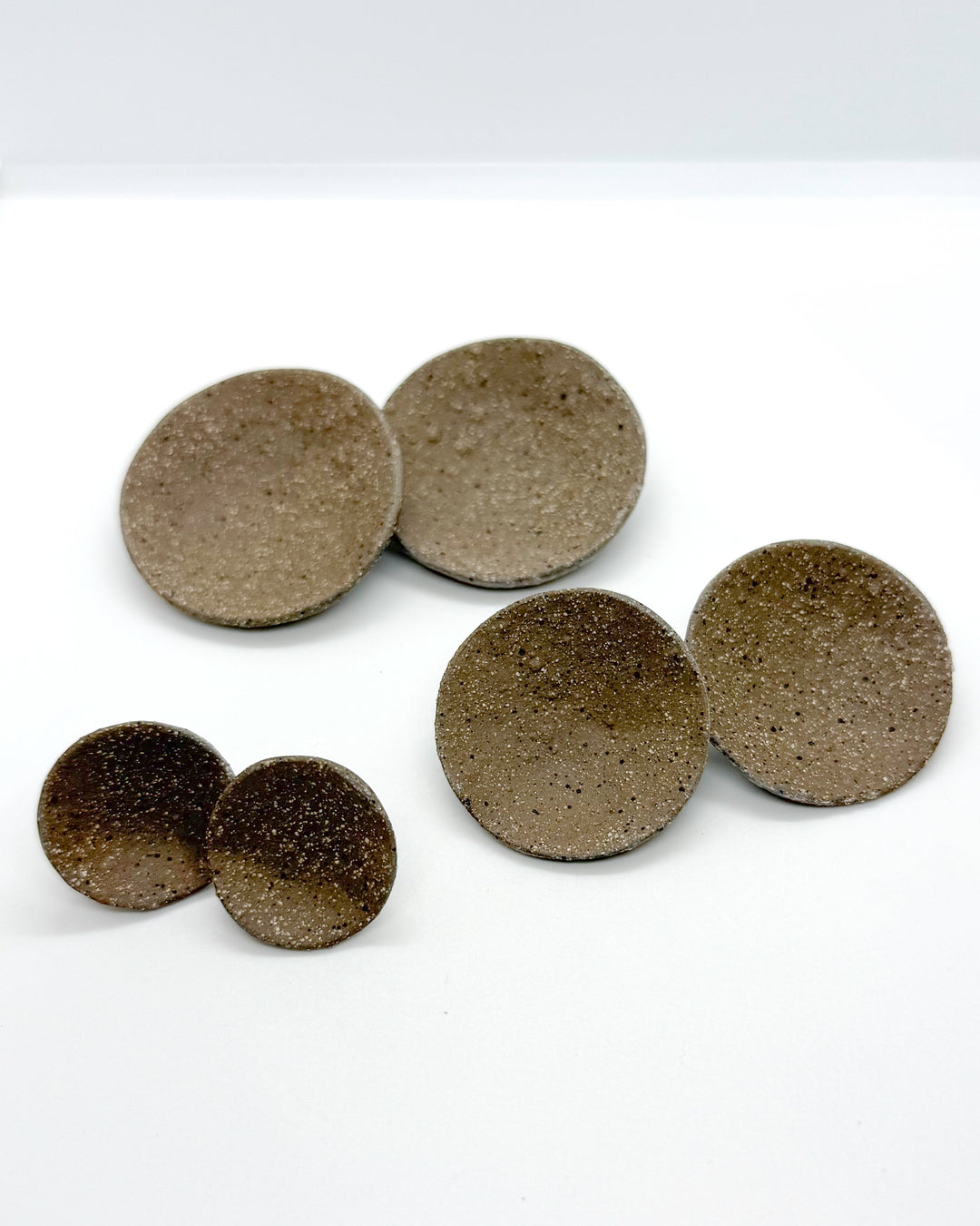 Set of six round ceramic earrings with a speckled texture on a white background