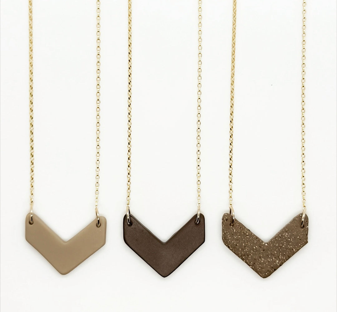 Three chevron-shaped necklaces on gold chains against a white background
