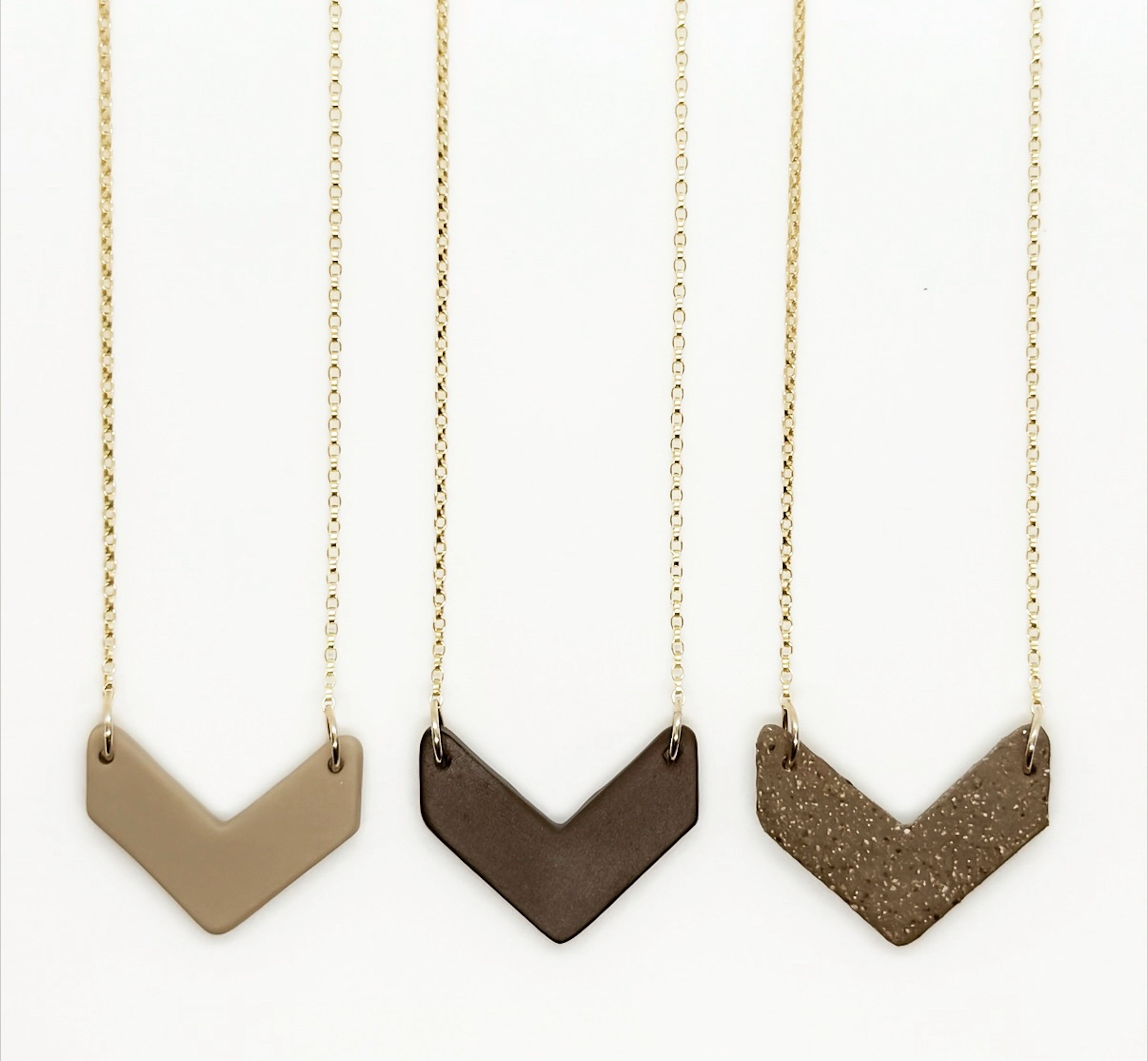 Three chevron-shaped necklaces on gold chains against a white background