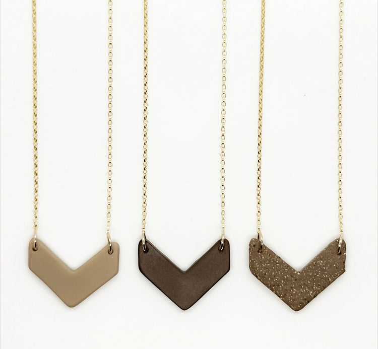 Three chevron-shaped necklaces on gold chains against a white background