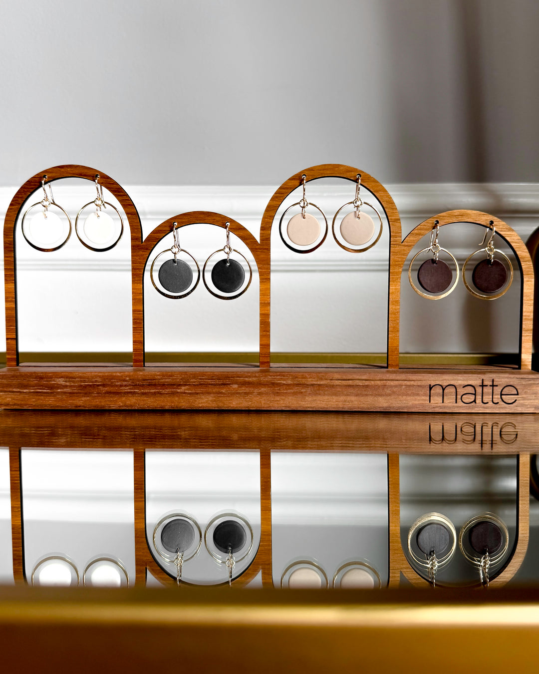 Wooden earring display rack with various earrings on a reflective surface.