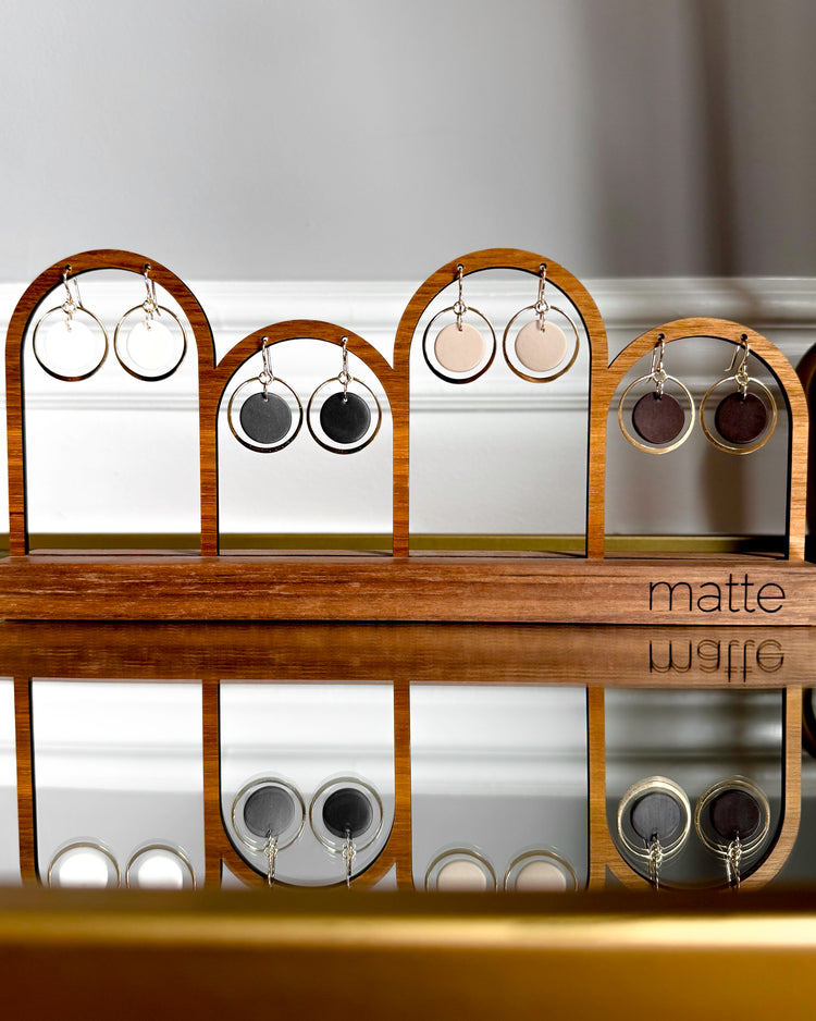 Wooden earring display rack with various earrings on a reflective surface.