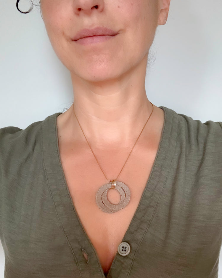 Person wearing a green shirt with a necklace featuring a circular pendant on a plain background