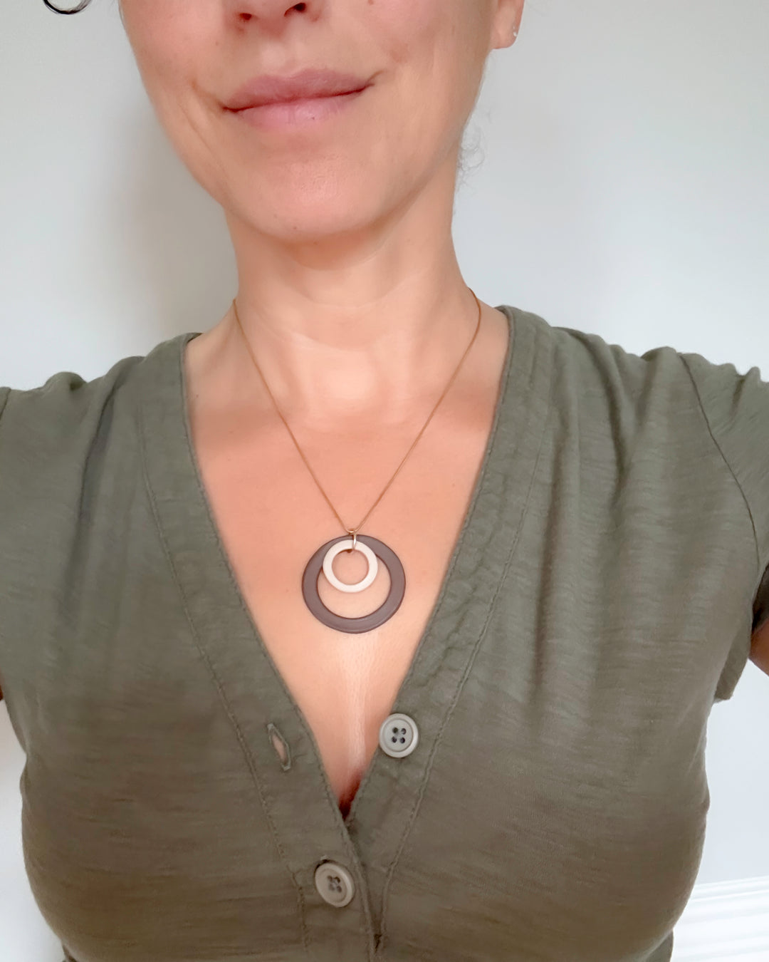 Person wearing a green top with a necklace featuring circular pendants on a plain background