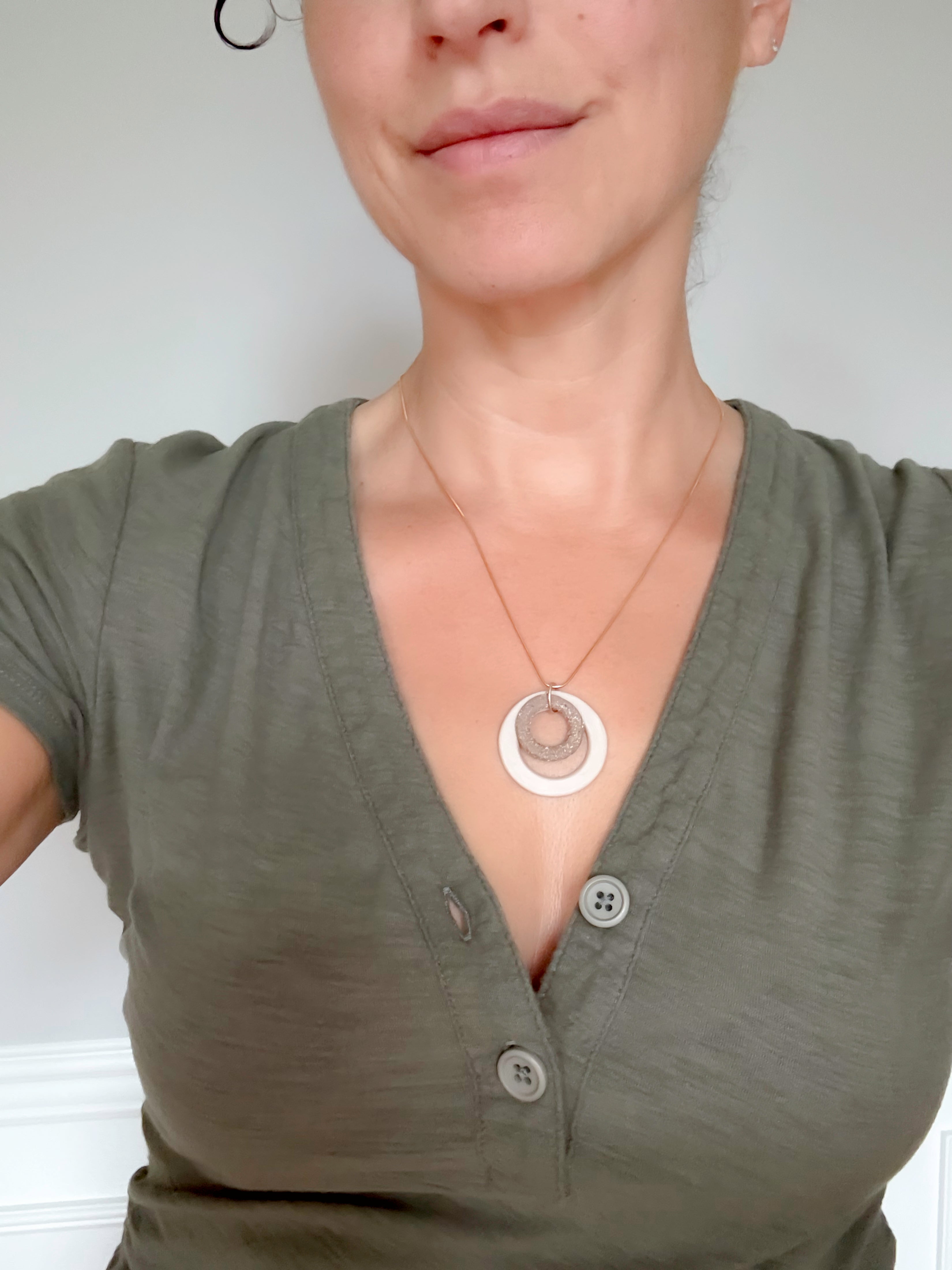 Person wearing a green shirt with a necklace featuring a circular pendant.
