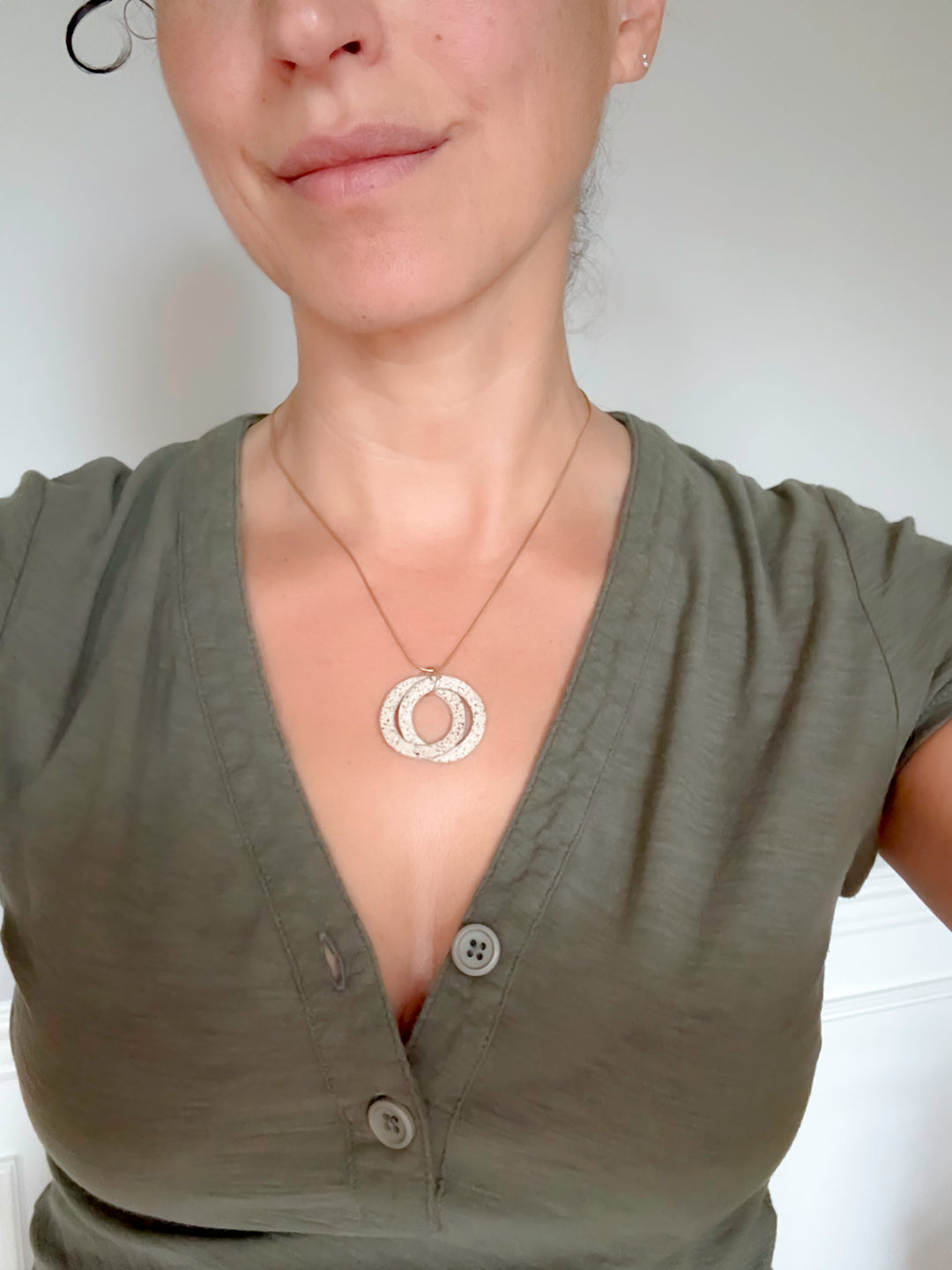 Person wearing a green shirt with a necklace featuring a circular pendant against a plain background