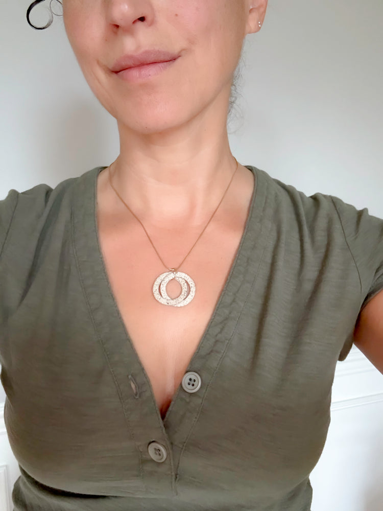 Person wearing a green shirt with a necklace featuring a circular pendant against a plain background