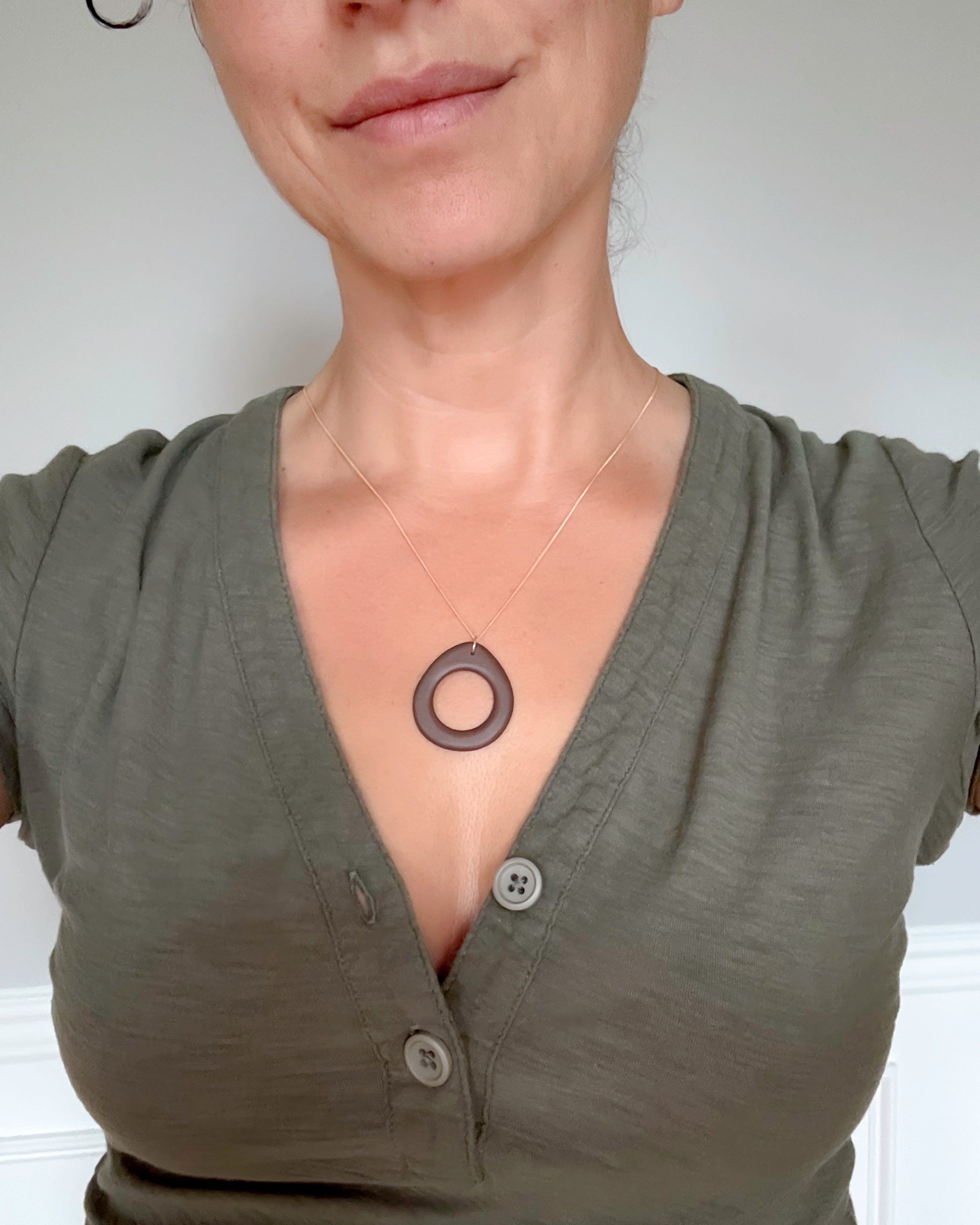 Person wearing a green shirt with a necklace featuring a circular pendant against a plain background