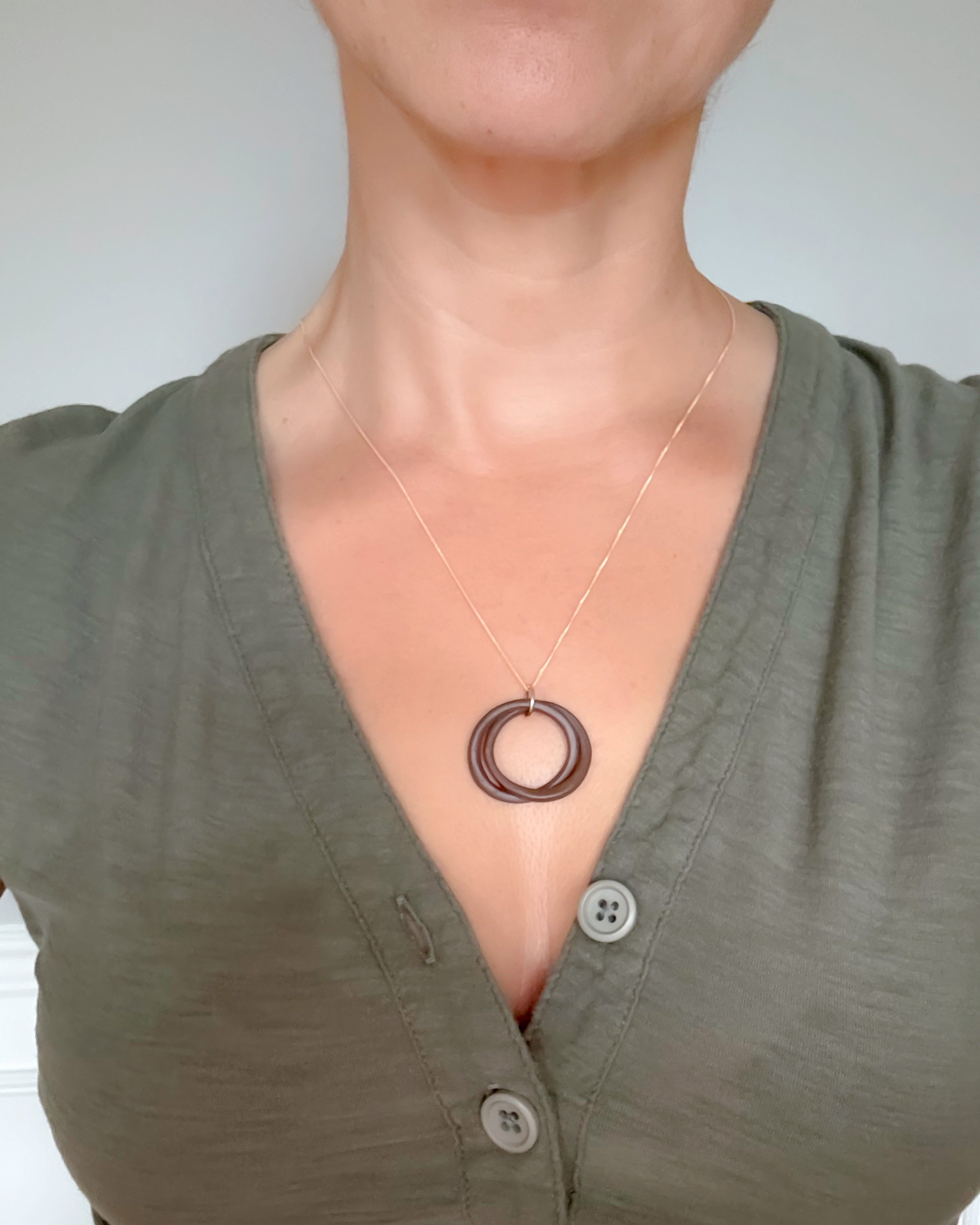 Person wearing a green shirt with a necklace featuring a circular pendant.