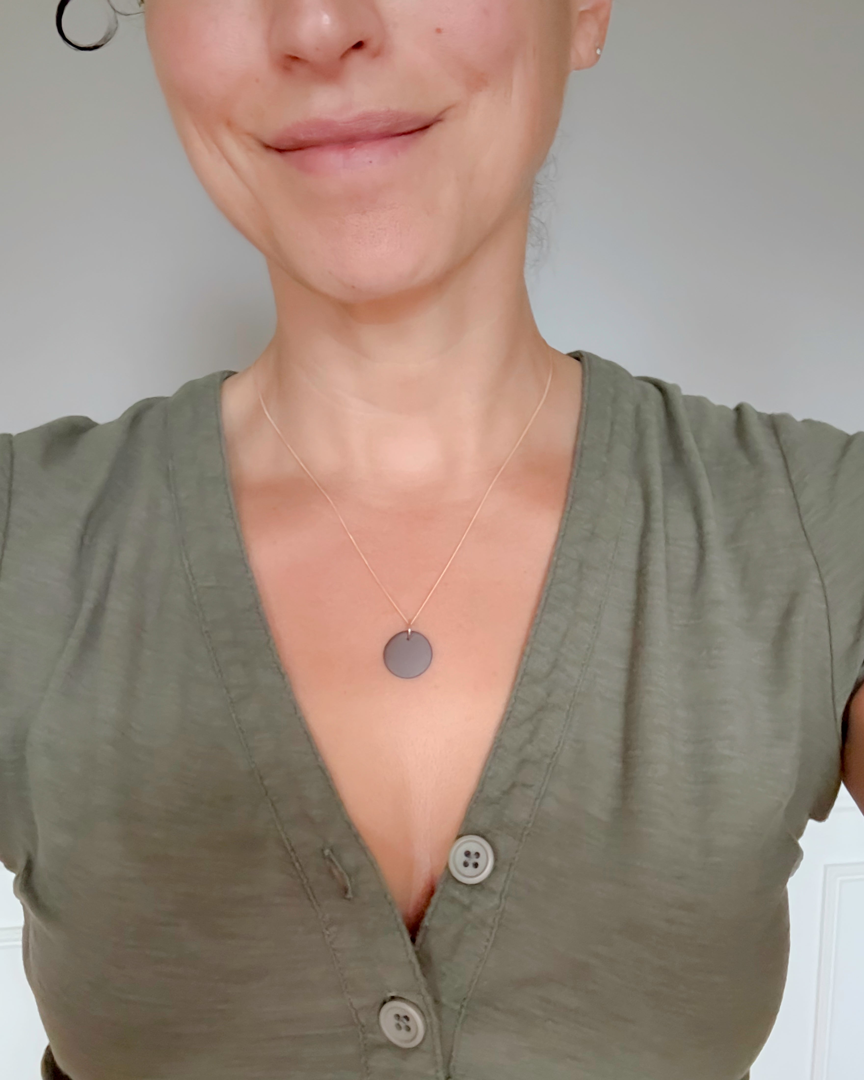Person wearing a green shirt with a necklace featuring a round pendant.