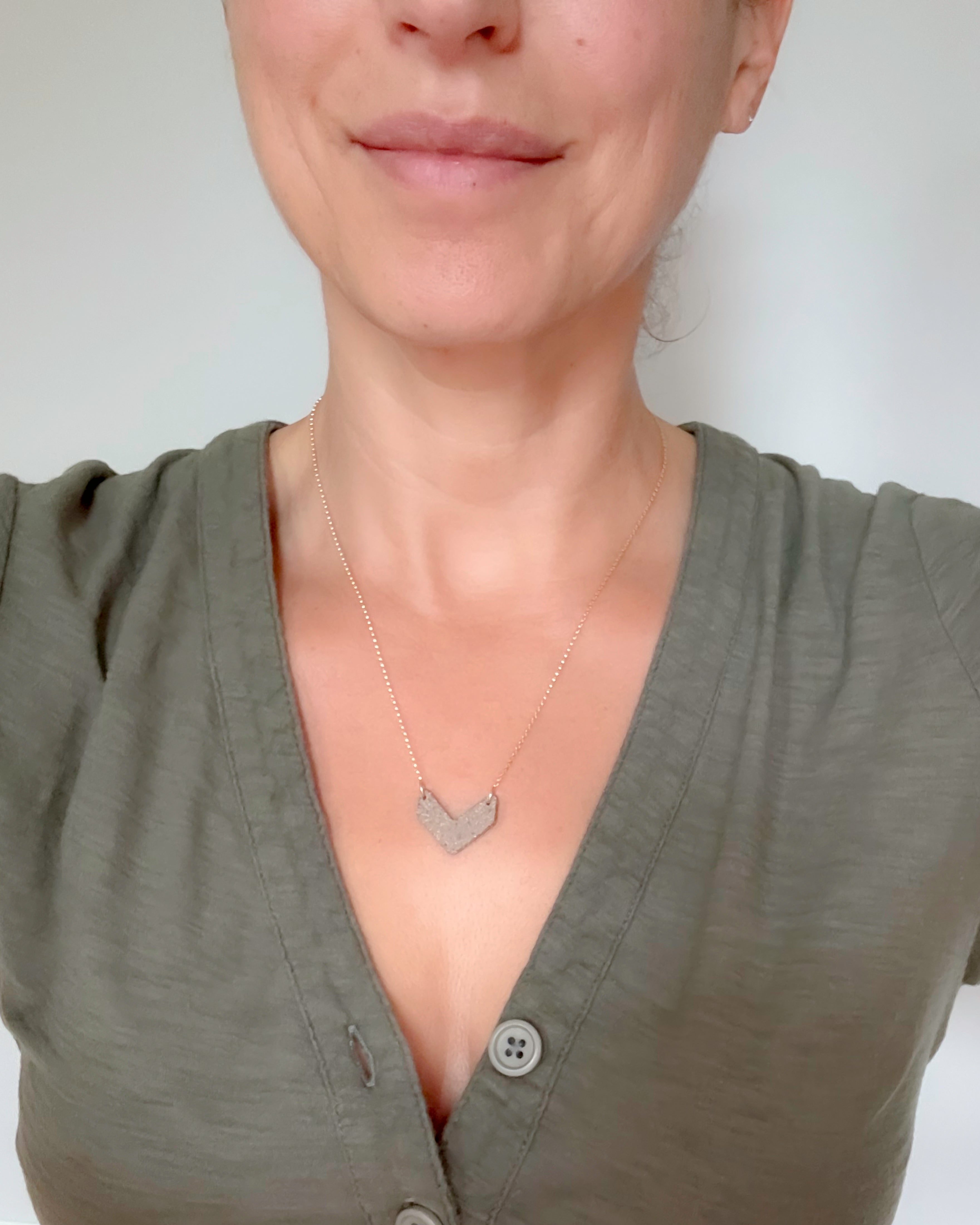 Woman wearing a green shirt with a necklace featuring a heart-shaped pendant on a plain background