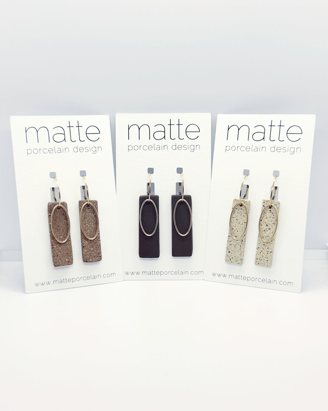 Three pairs of earrings on 'matte porcelain design' cards against a white background