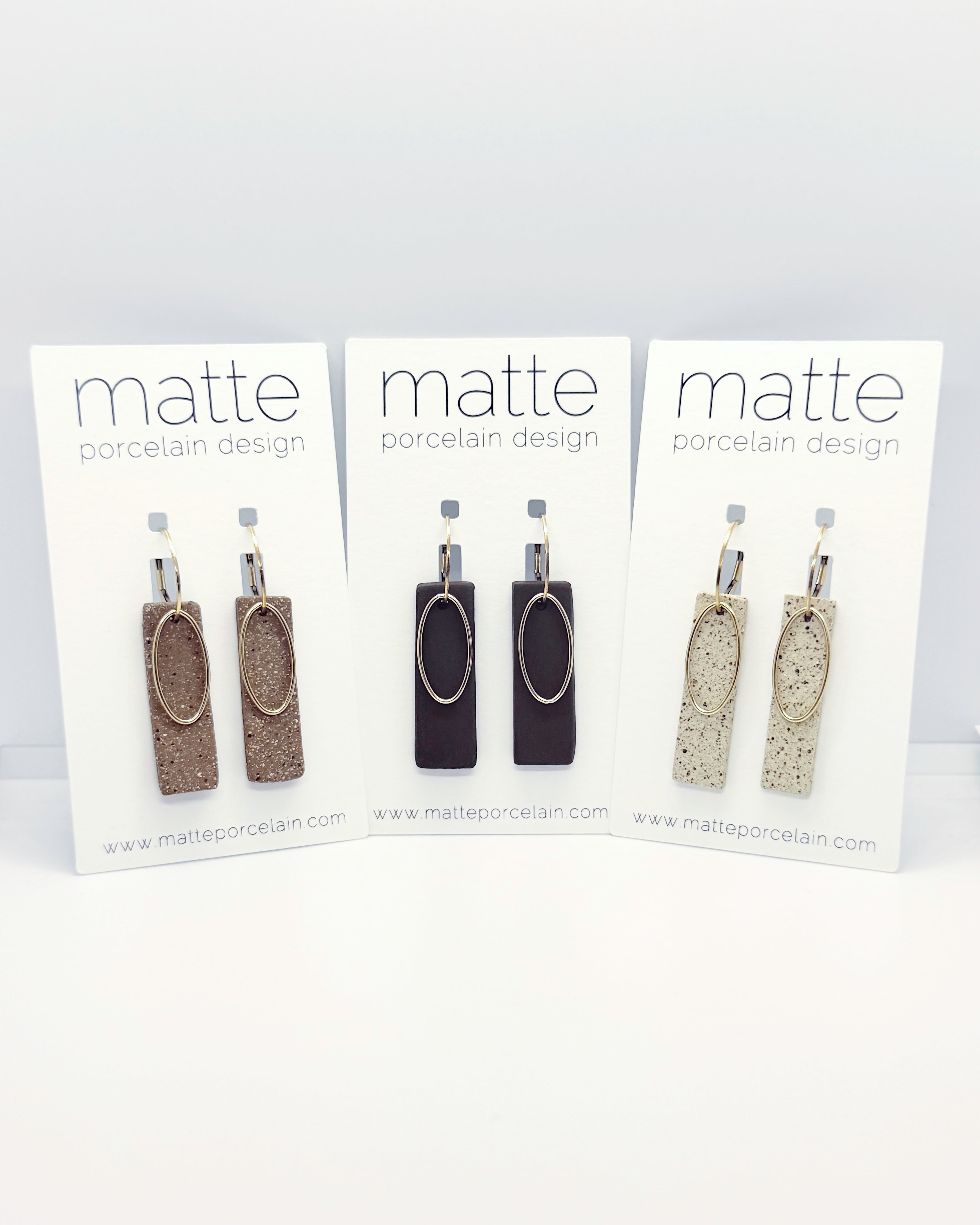 Three pairs of earrings on 'matte porcelain design' cards against a white background