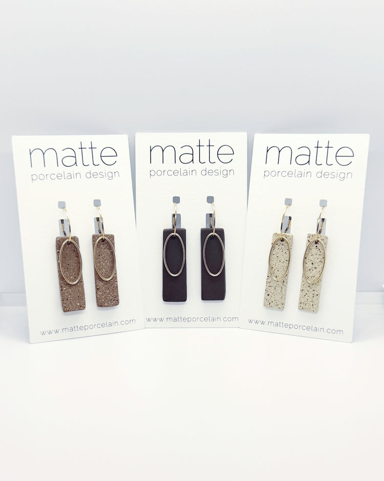 Three pairs of earrings on 'matte porcelain design' cards against a white background