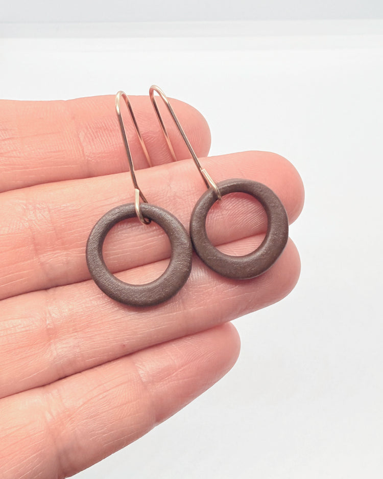 Pair of round earrings held between fingers against a neutral background