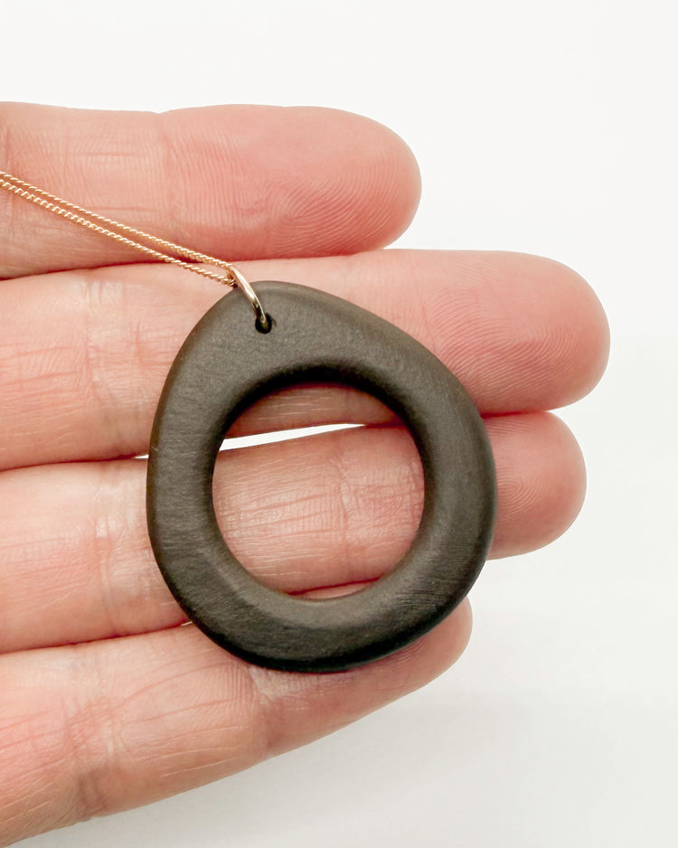 Hand holding a necklace with a large circular pendant against a white background