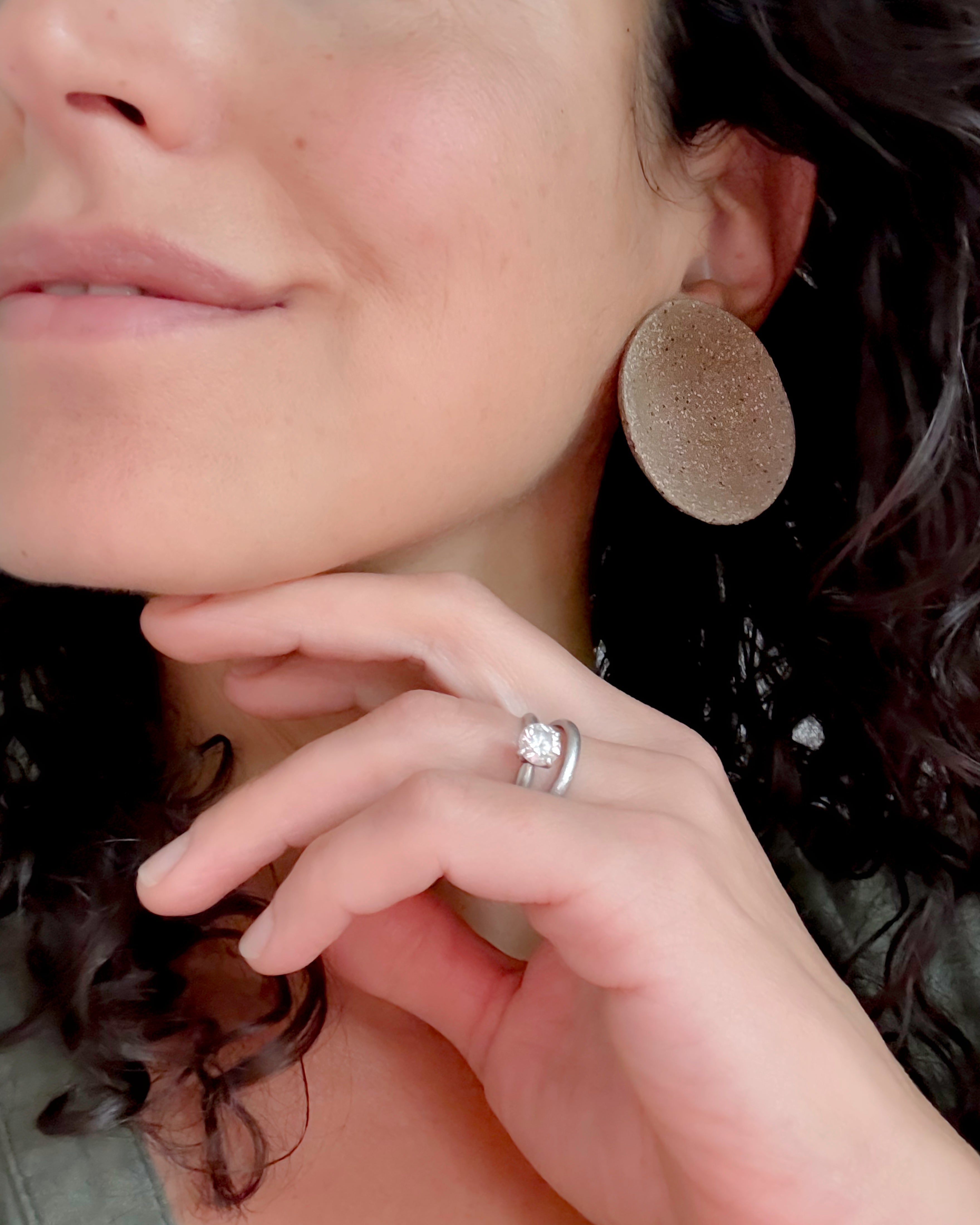 Close-up of a woman wearing a round earring and ring with a diamond.
