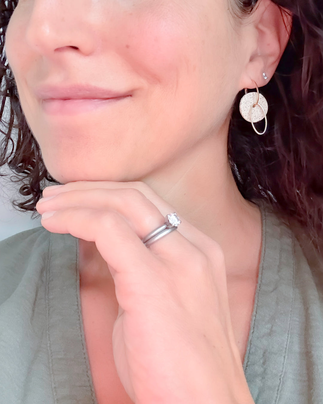 Close-up of a person wearing earrings and a ring, with a neutral background