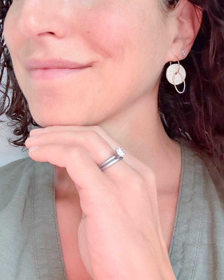 Close-up of a person wearing earrings and a ring, with a neutral background
