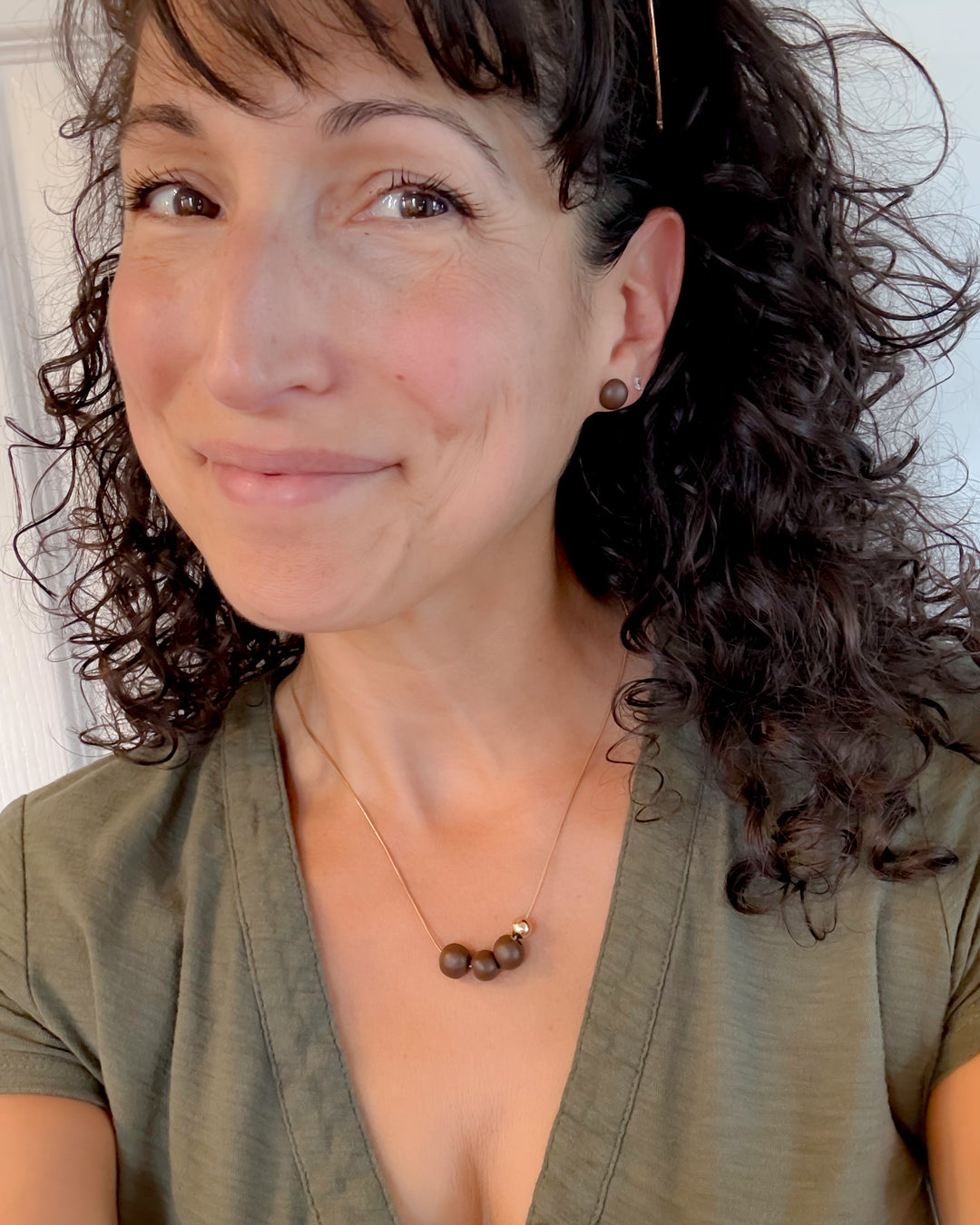 Woman with curly hair wearing a green top and necklace against a neutral background
