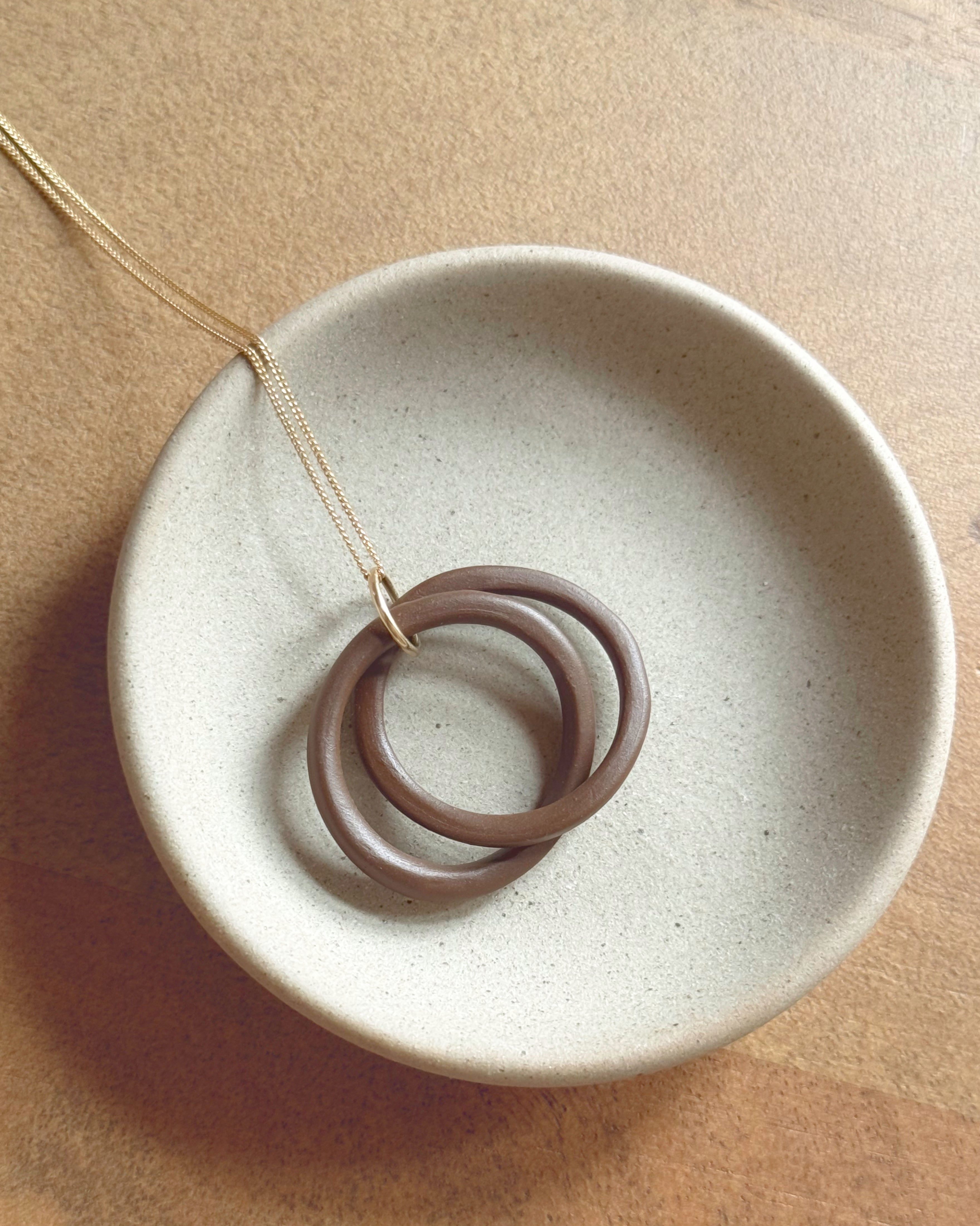Ceramic dish with a necklace featuring interlocking rings on a beige background
