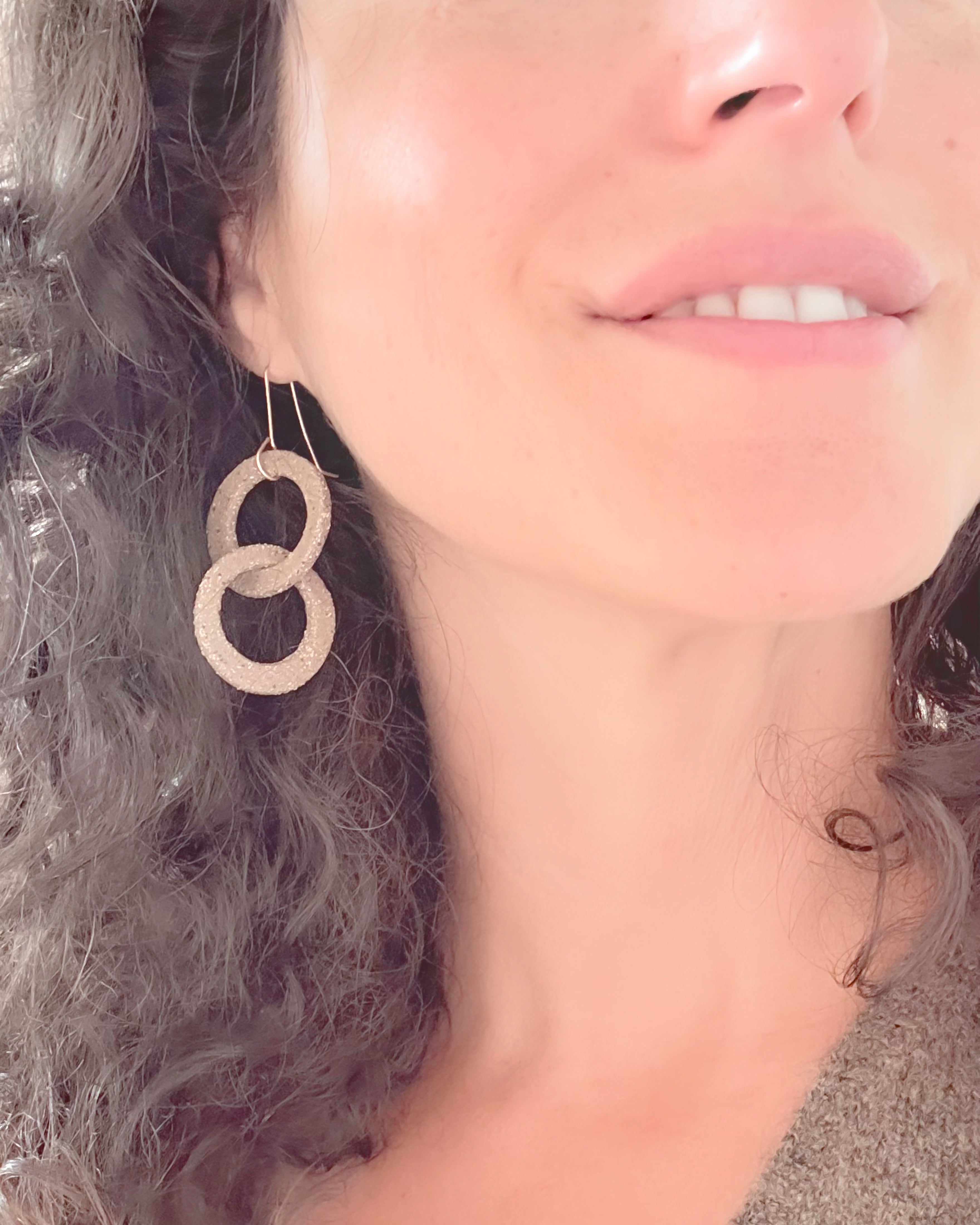Close-up of a woman wearing stoneware hoop earrings with a neutral background