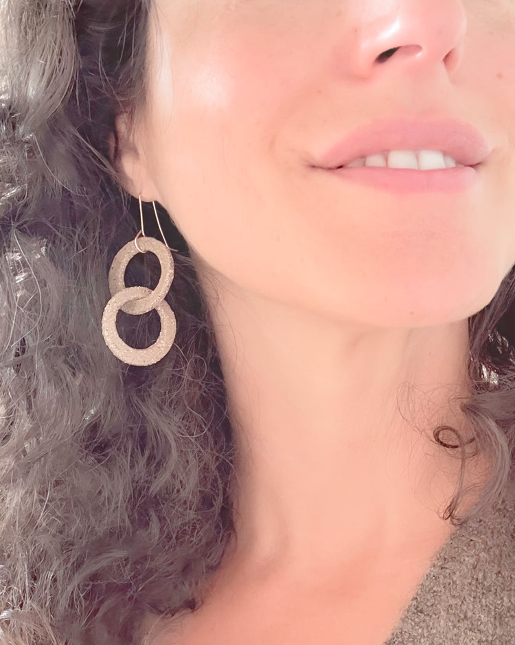 Close-up of a woman wearing stoneware hoop earrings with a neutral background