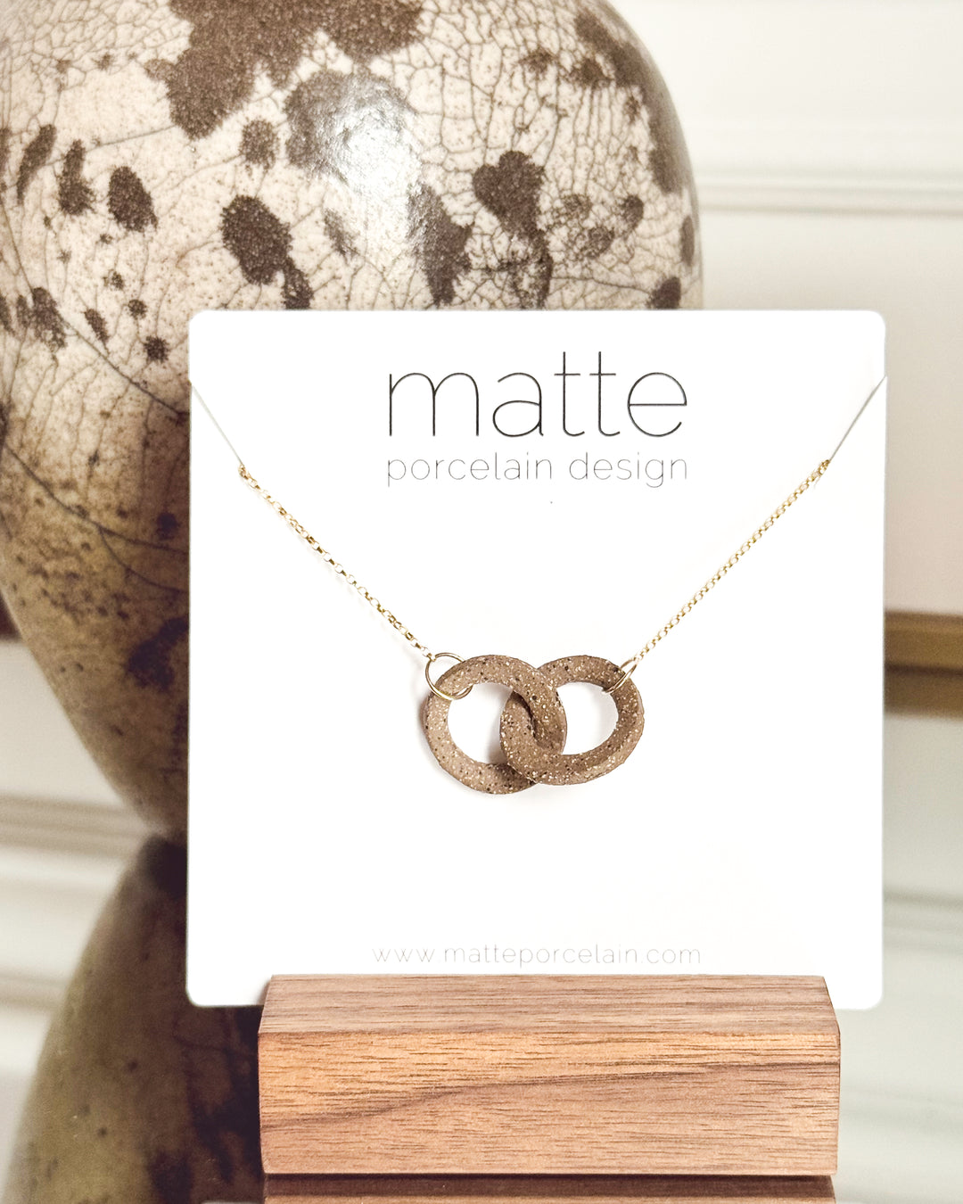 Necklace with interlocking rings on a 'matte porcelain design' card with a textured background.