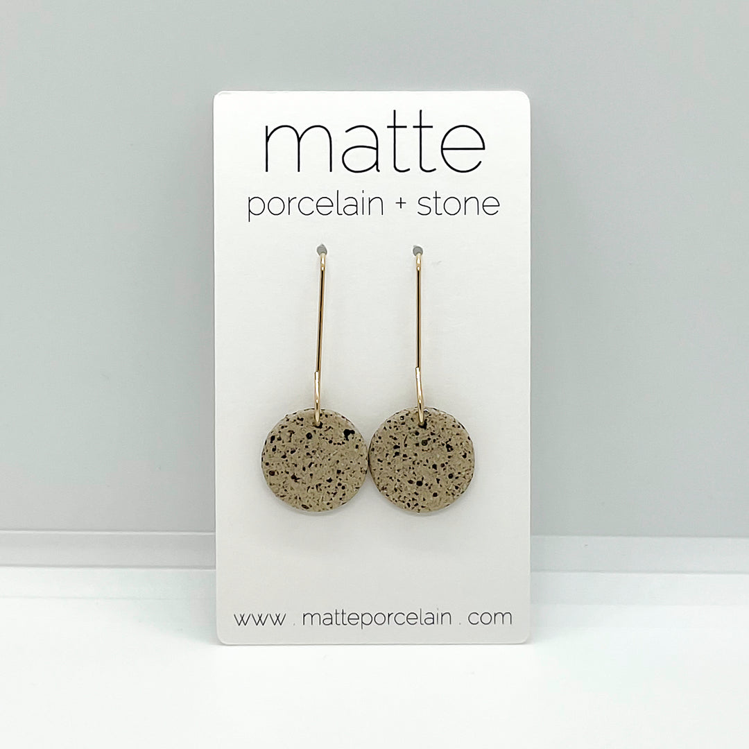 Pair of round earrings on a 'matte porcelain + stone' branded card against a gray background.