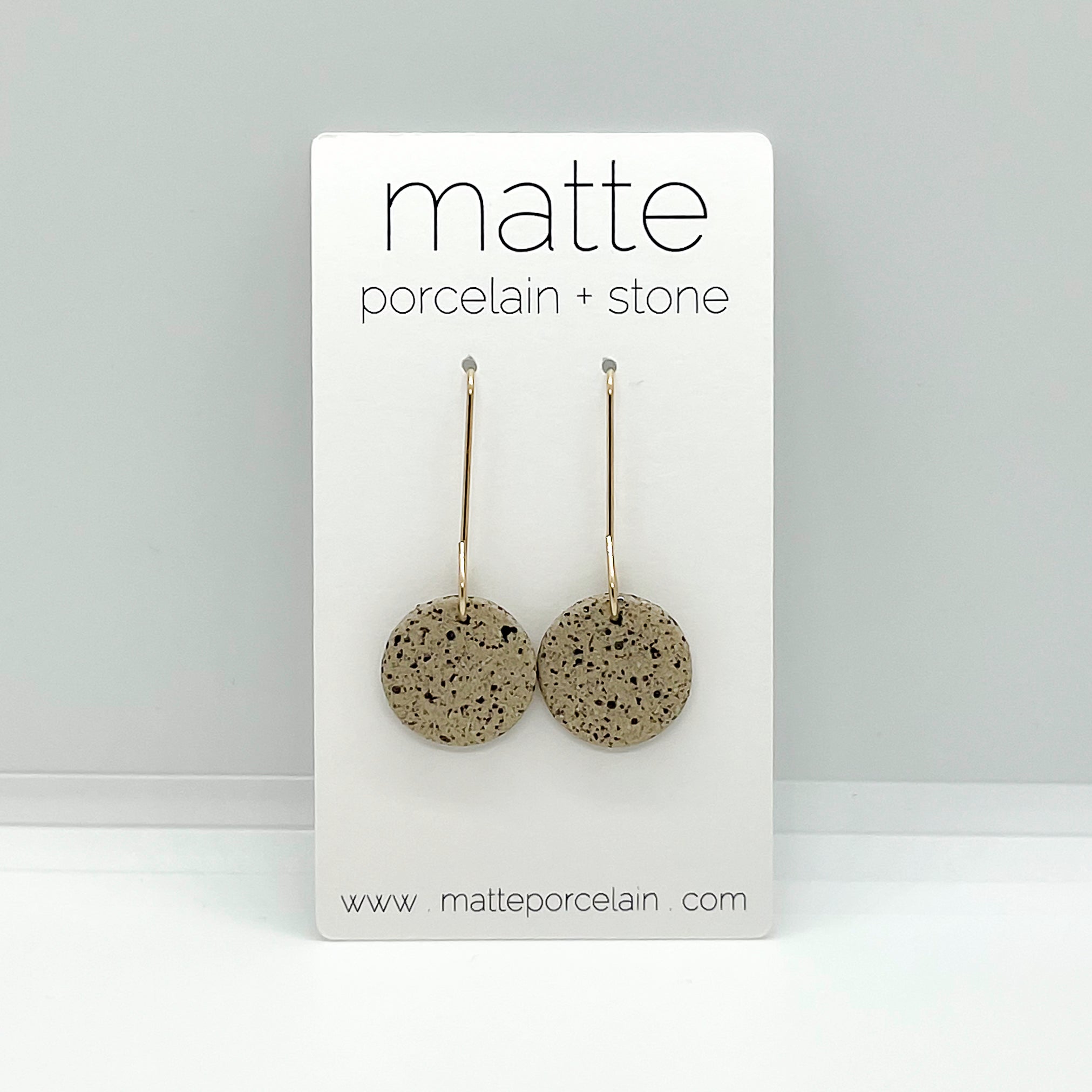 Pair of round earrings on a 'matte porcelain + stone' branded card against a gray background.