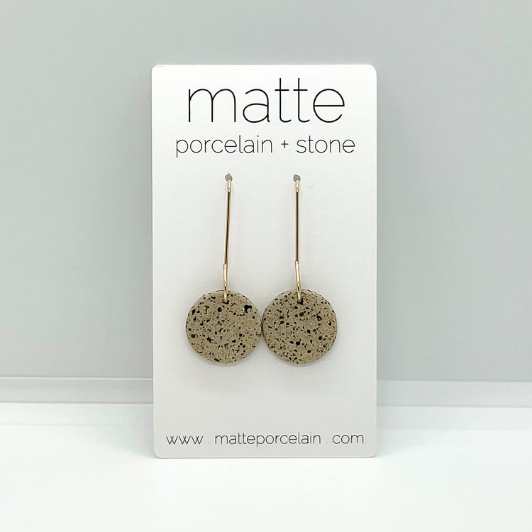 Pair of round earrings on a 'matte porcelain + stone' branded card against a gray background.